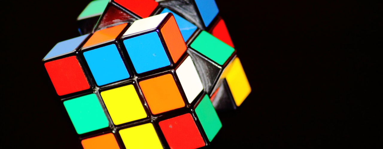 Ein Rubik's Cube, teilweise gedreht, mit den typischen Farben Rot, Blau, Gelb, Grün, Weiß und Orange, auf einem schwarzen Hintergrund