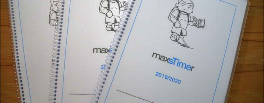 Drei Schülerplaner mit der Aufschrift 'maxsTimer 2019/2020' und einem gezeichneten Schüler auf dem Cover liegen auf einem Holztisch