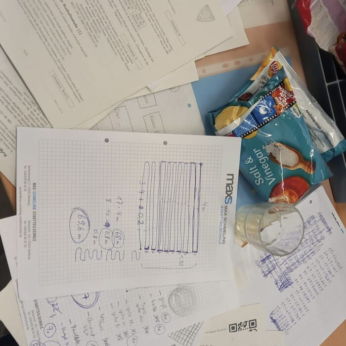 Ein Tisch mit beschrifteten Blättern, einem Glas, Snacks und mathematischen Skizzen, darunter Papier mit dem Logo der Max-Schmeling-Stadtteilschule