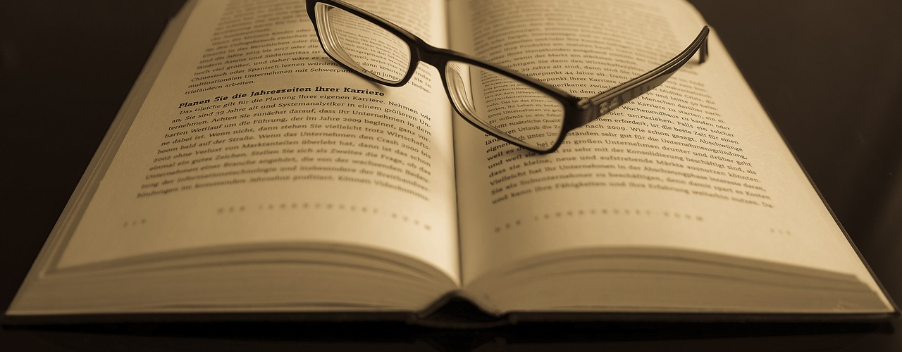 Ein aufgeschlagenes Buch auf dem eine schwarze Brille liegt
