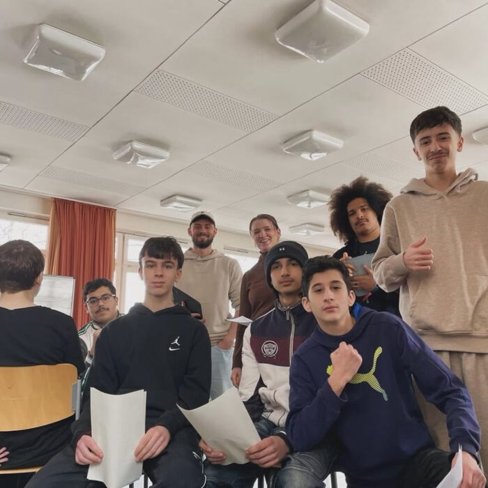 Gruppe von Jugendlichen steht mit Noten- und Textblättern im Musikraum