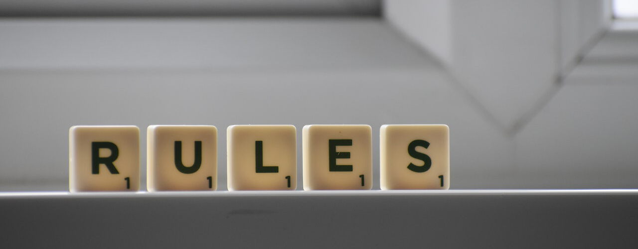 Scrabble-Steine bilden das Wort 'RULES' auf einer Fensterbank, mit einem hellen Fenster im Hintergrund