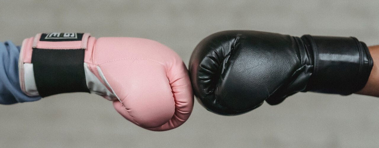 Zwei Boxhandschuhe berühren sich vor grauem Hintergrund